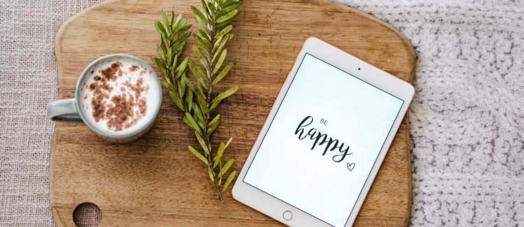 une tablette qui affiche le message "happy" pour donner le sourire à une entrepreneuse qui cumule salariat et freelancing